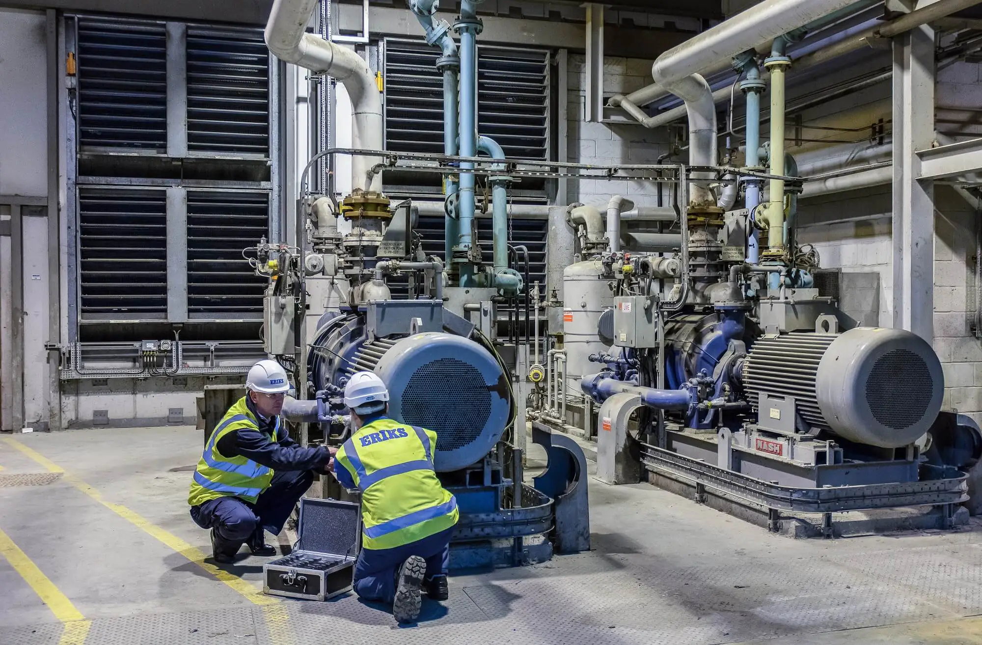 Two ERIKS technicians perform field service management, inspecting a "CONDENSER AIR EXTRACTION PUMP 10-PP-020" and "NASH" machinery with a tool kit in a factory. "LIVE" box.