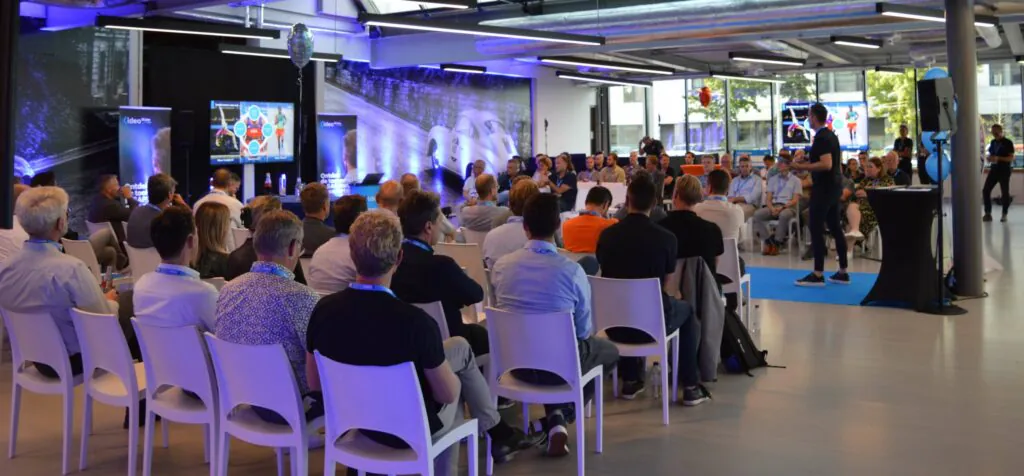 A male presenter addresses an audience in a modern conference room. Screens show "Ideo". A banner reads: "Ideo Ontdek de toekomst met SAP". This is an **SAP FSM** conference.