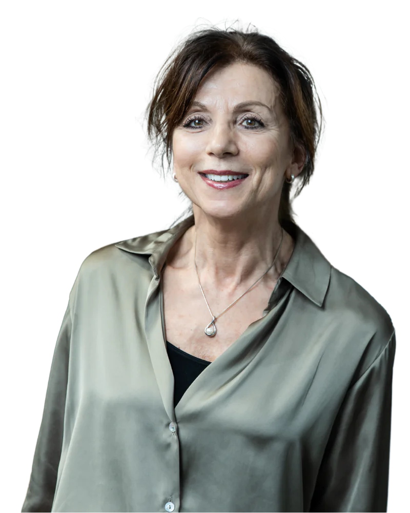 Middle-aged woman smiles, looking forward, wearing a sage collared shirt and teardrop pendant against a white background.