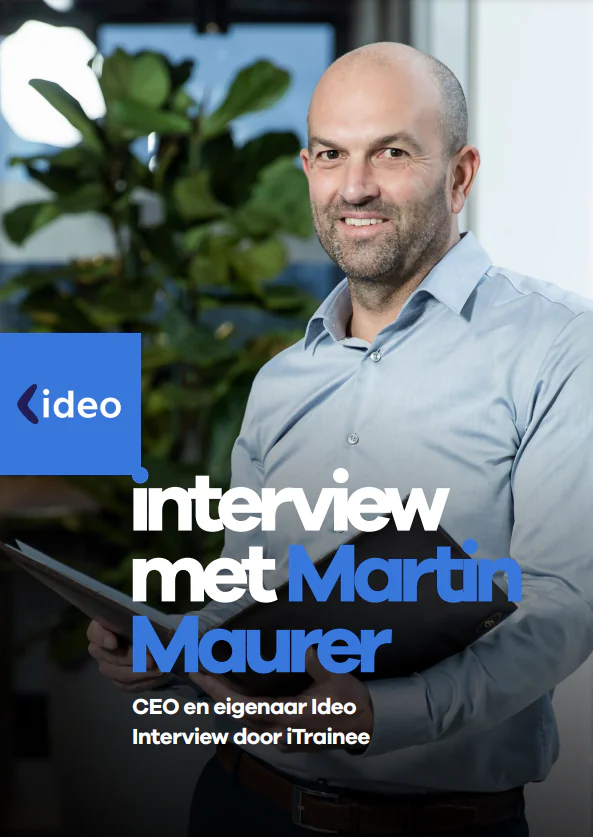 Een glimlachende man houdt een map vast in een kantooromgeving; hij staat symbool voor expertise in SAP FSM en asset management. Tekst: ideo, interview met Martin Maurer, CEO en eigenaar Ideo, Interview door iTrainee