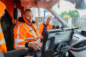 Twee monteurs in oranje werkkleding gebruiken een Panasonic-tablet voor field service management terwijl ze in een bestelwagen zitten en samen naar het scherm kijken.