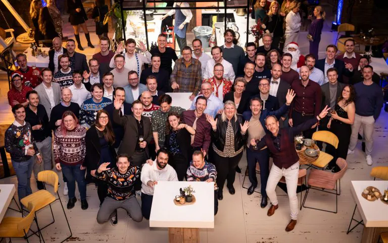 Een grote groep collega's viert een kerstborrel in een sfeervolle evenementenruimte, waarbij ze poseren voor een foto voor effectief asset management binnen het bedrijf.