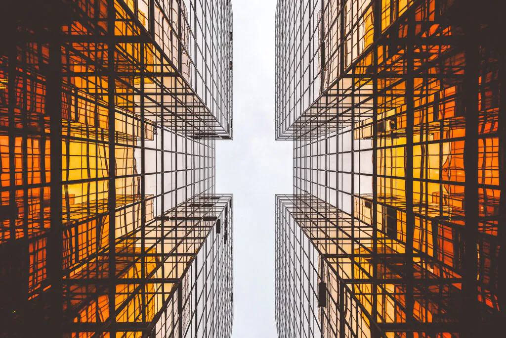 Vier moderne wolkenkrabbers rijzen op, hun glazen gevels reflecteren een warm oranje licht tegen de hemel, waardoor een symmetrisch stedelijk perspectief ontstaat dat uitstekend past bij complex asset management.