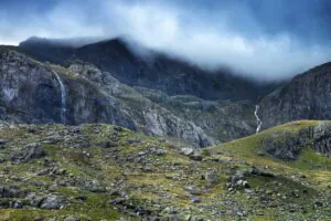 Watervallen kletteren langs ruige, rotsachtige bergen die gedeeltelijk in mist gehuld zijn, terwijl ze een uitdagend landschap creëren dat zelfs voor **asset management** in de natuur een complexe omgeving vormt.