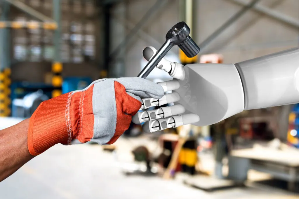 Een menselijke hand in een werkhandschoen geeft een dopsleutel door aan een robotarm ter ondersteuning van field service management in een industriële werkplaats.