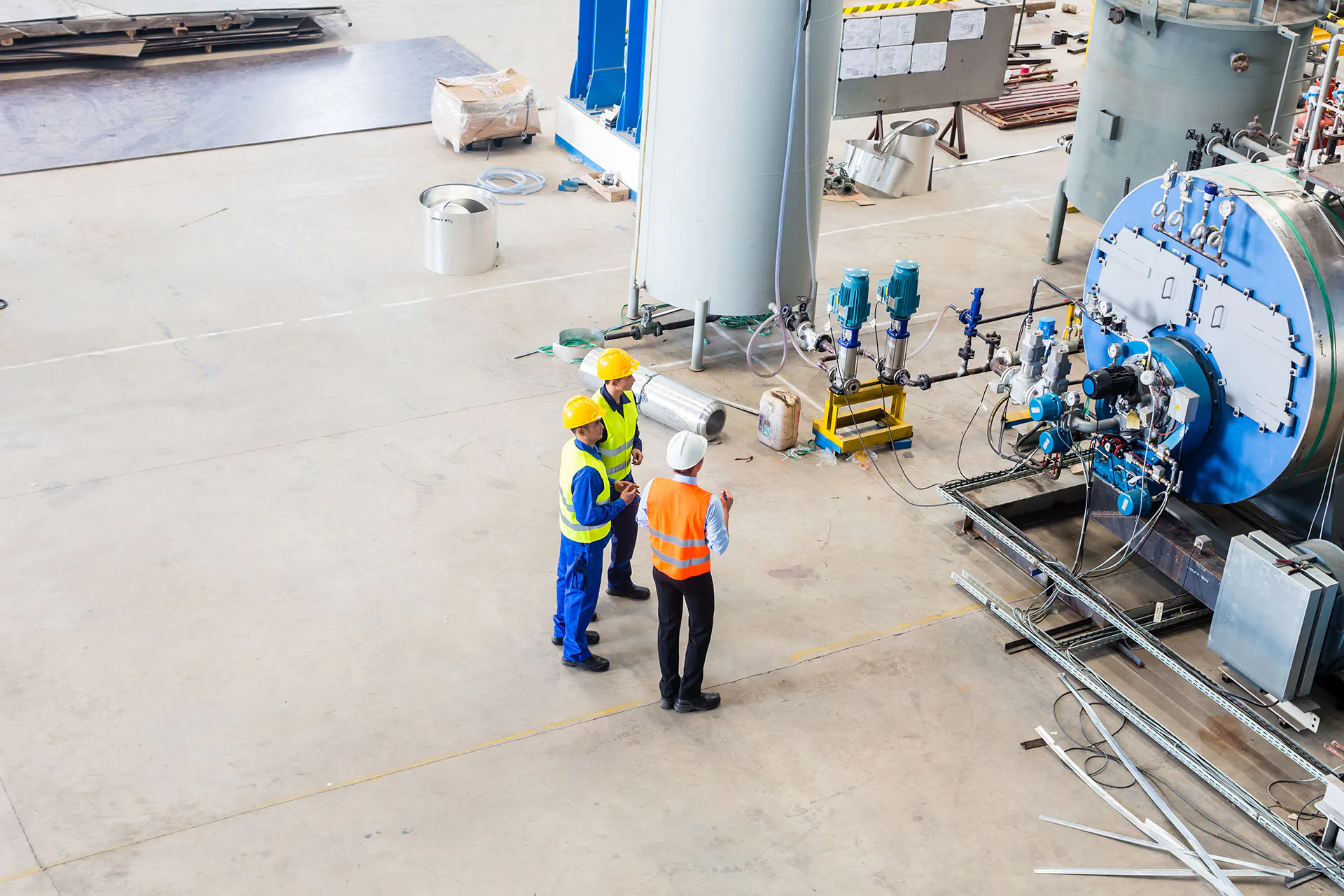 Drie technici in beschermende kleding inspecteren industriële machines in een ruime werkplaats, waarbij ze toezicht houden op de operatie en onderhoud voor effectief field service management in de fabriekshal.