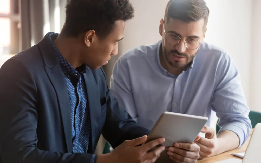 Twee zakenlieden bestuderen aandachtig een tablet tijdens een overleg over SAP FSM-oplossingen in een professionele kantooromgeving, waarbij ze samenwerken om processen te optimaliseren.
