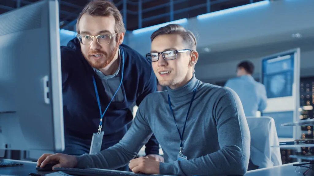 Twee technici bespreken data op een computerscherm in een modern kantoor, waarbij ze software voor SAP FSM gebruiken voor efficiënt beheer en analyse in een professionele werkomgeving.