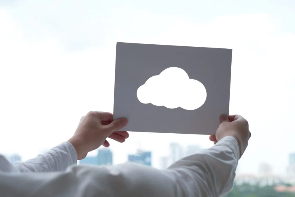Twee handen houden een vel papier vast met een uitgesneden wolkvorm, waarbij ze de lucht en stad op de achtergrond inkaderen als symbool voor moderne SAP FSM cloudtechnologie.
