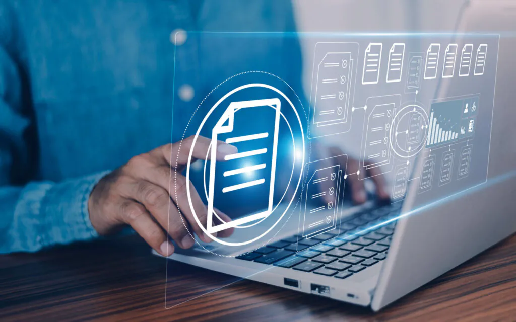 Een persoon bedient een laptop met een blauw, digitaal interface voor asset management, waarbij documenticonen en grafieken boven het toetsenbord verschijnen om digitale werkstromen en procesbeheer te visualiseren.