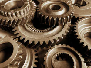 Verschillende metalen tandwielen liggen gestapeld, wat het asset management en industriële processen symboliseert, in een close-up opname met een sepia-kleurtoon die de textuur van de machineonderdelen benadrukt.