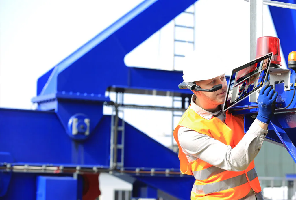 Een technicus met AR-bril voert onderhoud uit aan een blauwe industriële machine met behulp van SAP FSM voor efficiënt field service management. Tekst op scherm: "replace cable".