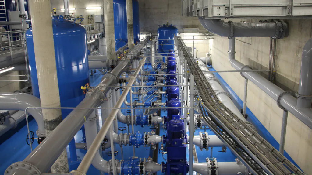 Blauwe pompen en leidingen verbinden grote tanks in een industriële installatie, waar SAP FSM processen helpen bij het optimaliseren van complex technisch asset management en onderhoud binnen deze infrastructuur.