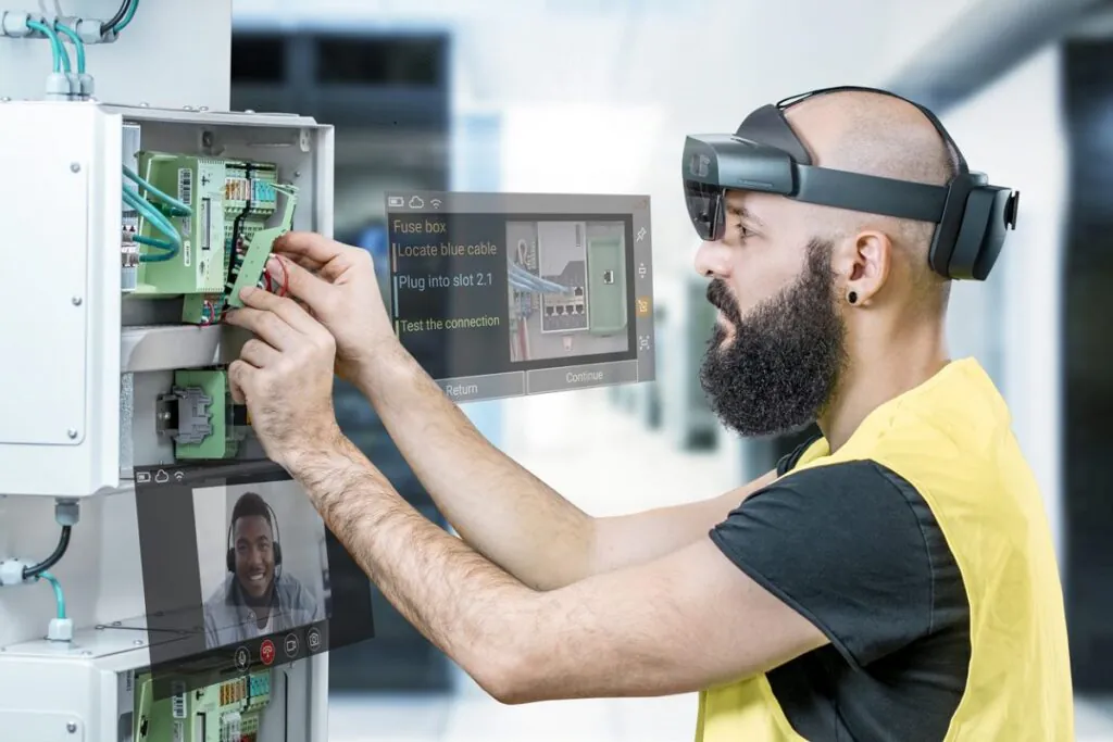 Een technicus draagt een AR-bril en voert onderhoud uit aan een verdeelkast met SAP FSM-ondersteuning, terwijl hij via een virtueel scherm videobelt. Tekst op het scherm: "Fuse box Locate blue cable Plug into slot 2.1 Test the connection Return Continue