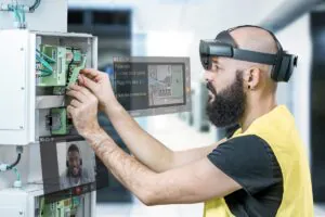 Een technicus draagt een AR-bril en voert onderhoud uit aan een verdeelkast met SAP FSM-ondersteuning, terwijl hij via een virtueel scherm videobelt. Tekst op het scherm: "Fuse box Locate blue cable Plug into slot 2.1 Test the connection Return Continue