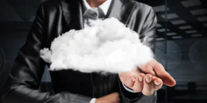 Een zakelijk geklede persoon houdt een witte, zwevende wolk vast in een handpalm tegen een donkere achtergrond, wat innovatieve oplossingen symboliseert zoals die binnen SAP FSM worden toegepast.