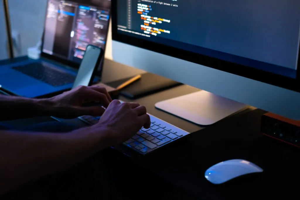 Handen typen op een toetsenbord terwijl ze code schrijven op een computerscherm in een donkere kantooromgeving, ondersteunend aan SAP FSM-processen. Tekst op scherm: "entation of a fight between 2 units" "unit.is_attack()" "unit.is_attack()" "unit.is_attack()" "unit.is_attack()" "unit.is_attack()