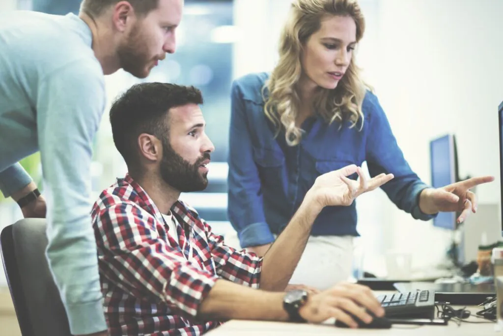 Twee mannen en een vrouw overleggen intensief bij een computer over SAP FSM-processen in een modern kantoor, waarbij één man het scherm aanwijst terwijl zij gezamenlijk samenwerken.