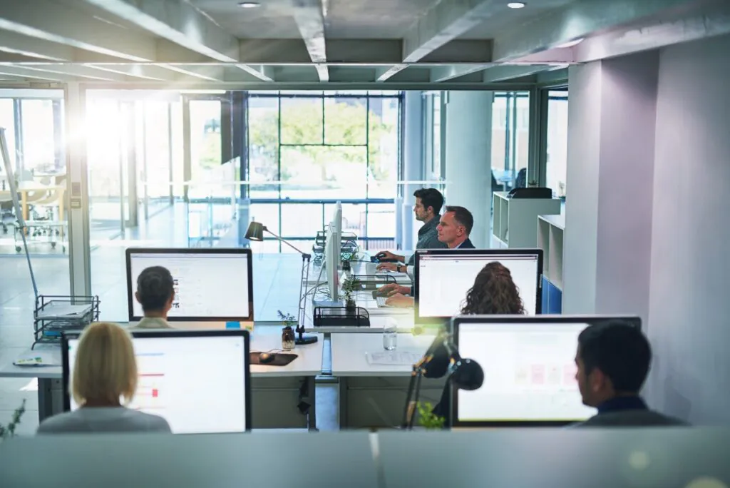 Kantoormedewerkers werken achter computers in een open kantooromgeving, waarbij ze moderne SAP FSM-oplossingen gebruiken voor efficiënt beheer van taken en dagelijkse werkzaamheden in een lichte, professionele setting.