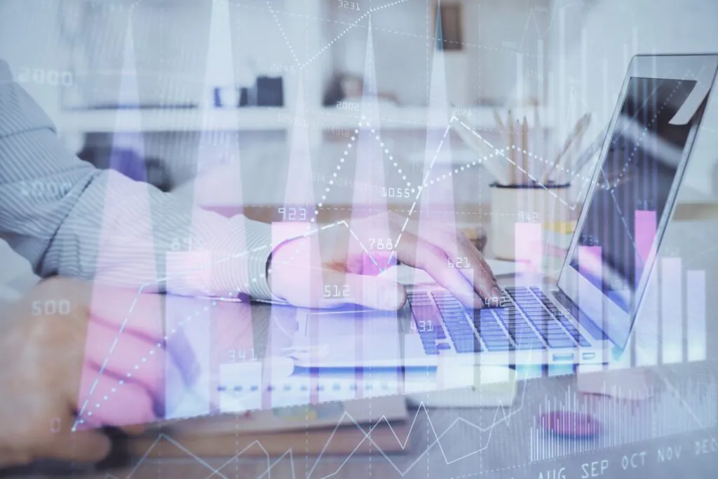 Een persoon typt op een laptop in een kantooromgeving terwijl digitale grafieken met sap technology en cijfers (o.a. 2000, 2245, 2002, 2028, 923, 788, 621, 512, 492, 431, 341, 0, 942, 734) over het scherm worden geprojecteerd.