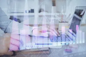 Een persoon typt op een laptop in een kantooromgeving terwijl digitale grafieken met sap technology en cijfers (o.a. 2000, 2245, 2002, 2028, 923, 788, 621, 512, 492, 431, 341, 0, 942, 734) over het scherm worden geprojecteerd.