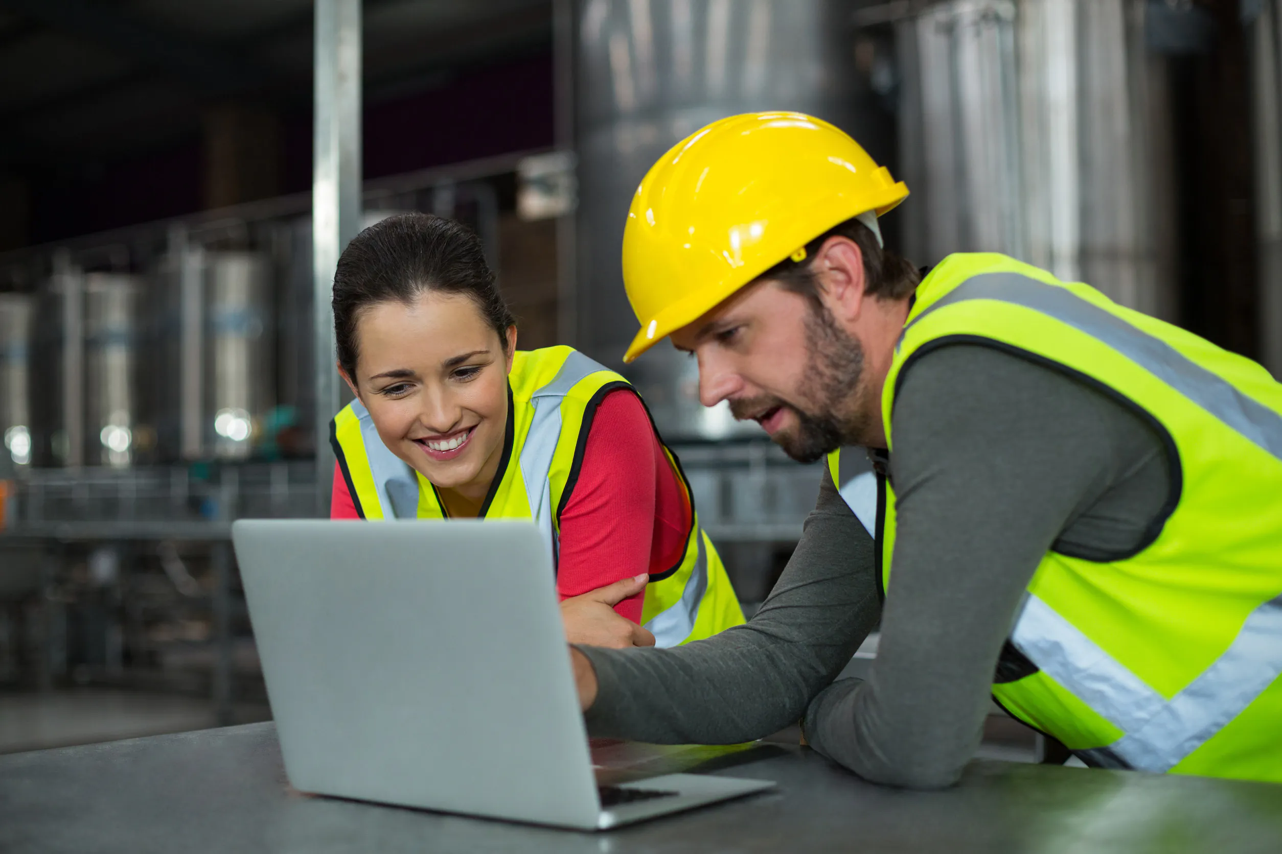 Twee technici in reflecterende vesten bekijken samen een laptop in een industriële omgeving om SAP FSM-processen te stroomlijnen en hun asset management en operationele efficiëntie te verbeteren.
